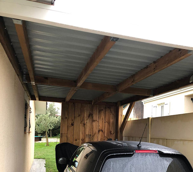 Carport en bois adossé avec toiture en bac acier protégeant une voiture